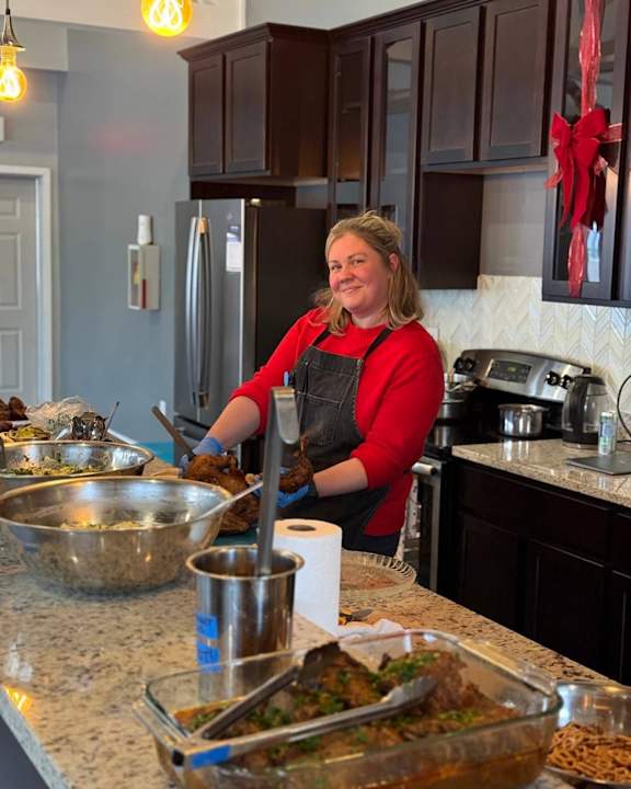 A woman in a red shirt and black apron is cooking in a kitchen.