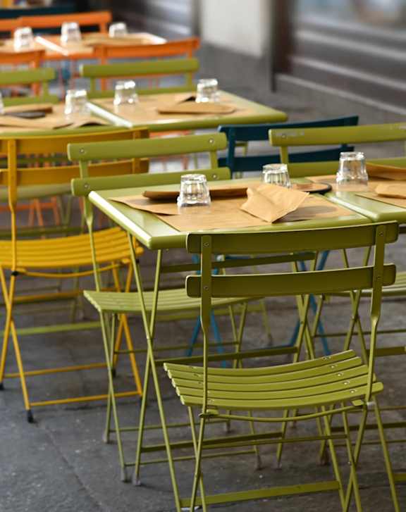 A row of green chairs with yellow legs and a table with a brown tablecloth and glasses on top.