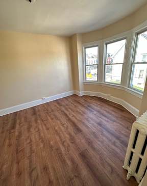 A room with wooden floors and a window overlooking a street.
