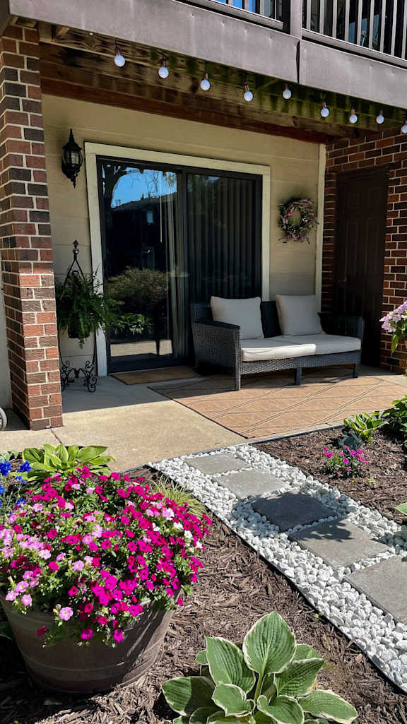 A patio with a couch and a table with a flower pot on the left and a flower pot on the right.
