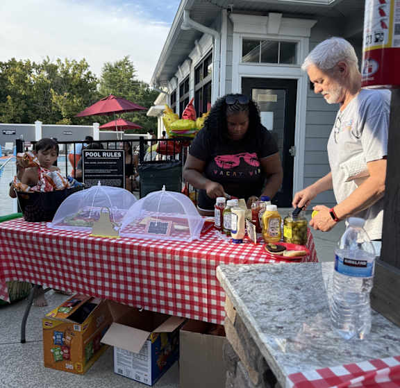 A man and a woman are standing behind a table with a red and white checkered tablecloth.