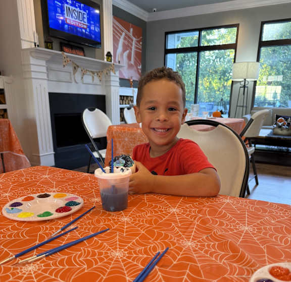A young boy is sitting at a table with paint and brushes.