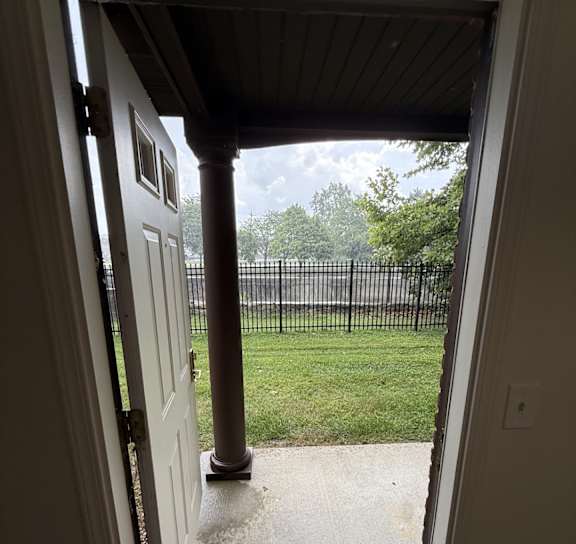 A white door is open to a porch with a black railing.