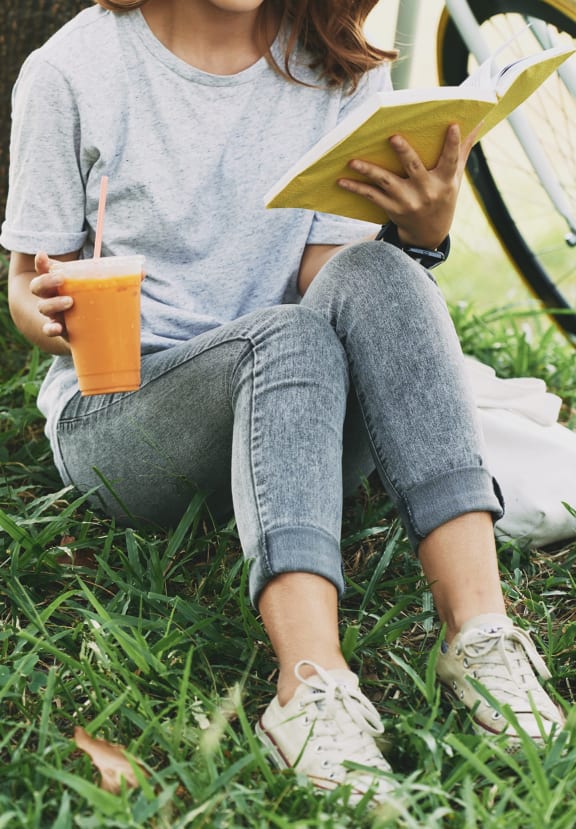 a woman sitting on the grass reading a book and drinking orange juice  at The Commons of McLean, Virginia