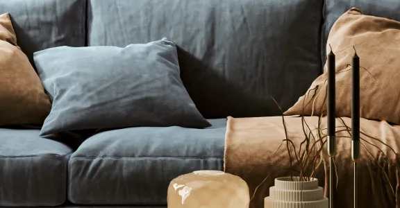 A blue couch with brown and blue pillows and a vase with plants on it.