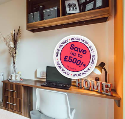 A bedroom with a bed, desk, and a sign offering savings on a hotel stay.