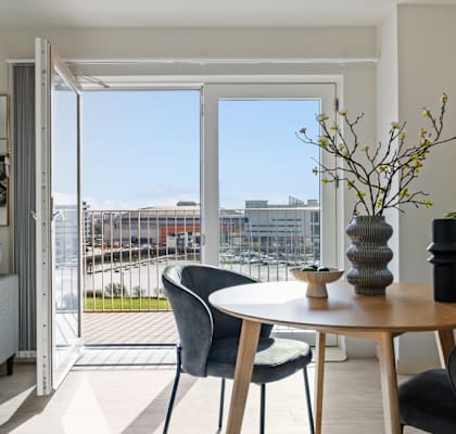A modern living room with a grey sofa, a round table with four chairs, and a view of the city.