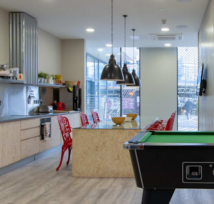 A billiard table is in the middle of a room with a kitchen area in the background.