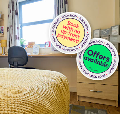 A bedroom with a bed, desk, and chair, with signs offering upgrades and deals.