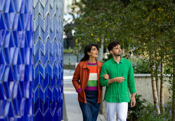 Two people walking in front of a blue patterned wall.