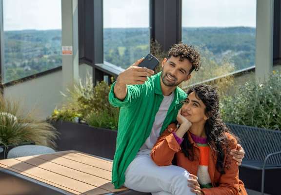 A man and woman are sitting on a balcony with a view of the city.