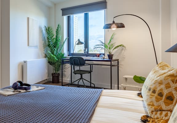 a bedroom with a bed and a desk and a living room with a window