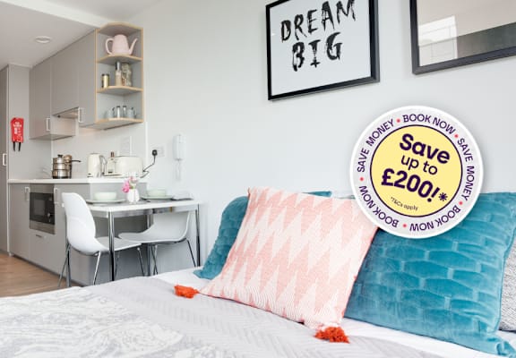 A bedroom with a bed, desk, and chair, with a sign that says "Save up to £2000".