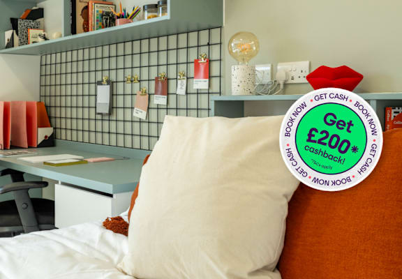 a bed with an orange pillow and a desk with a green sticker on it