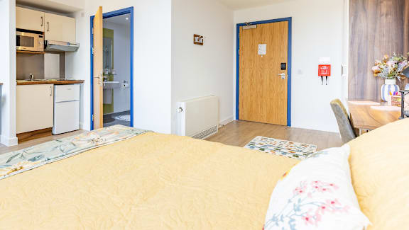 A bedroom with a bed, a chair, and a small kitchen area.