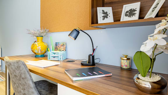 A room with a desk, chair, and a vase with flowers.