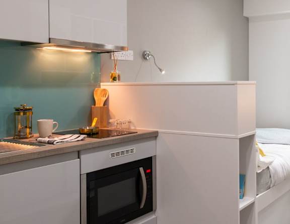 A small kitchen with a microwave oven and a bed in the same room.