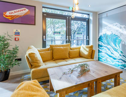 A living room with a yellow couch and a large wave mural on the wall.