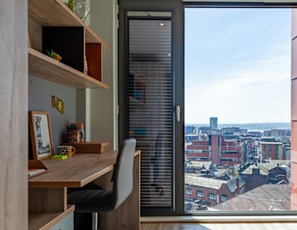 A room with a desk and a chair with a window that has a view of a city.