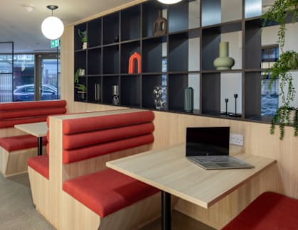 A room with a laptop on a table and red chairs.