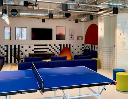 A ping pong table is in the middle of a room with a white wall that says "Welcome to HIGHLIGHT PARKGATE".