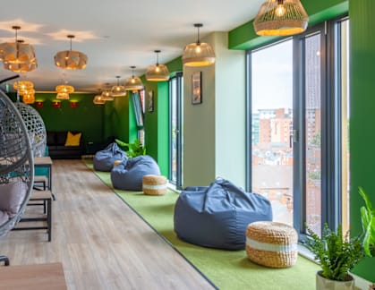 A room with green walls and a long wooden table with a hanging chair and bean bag chairs.