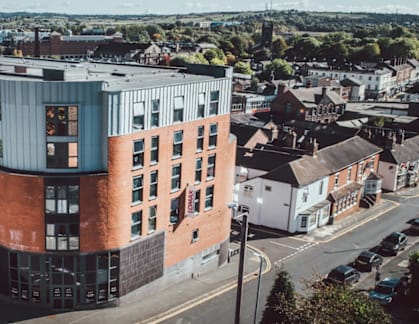 A modern building with a curved glass facade is situated in a town.