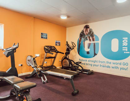 A gym with orange walls has a sign that says "GO FOR IT!".
