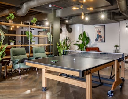 A ping pong table is in the middle of a room with a red couch and a green chair.