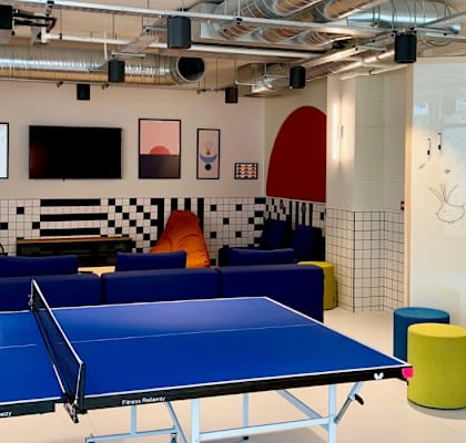 A ping pong table is in the middle of a room with a white wall that says "Welcome to HIGHLIGHT PARKGATE".