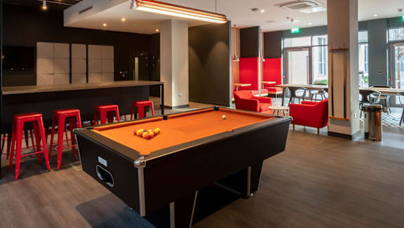 A pool table is in the middle of a room with a bar and a foosball table.
