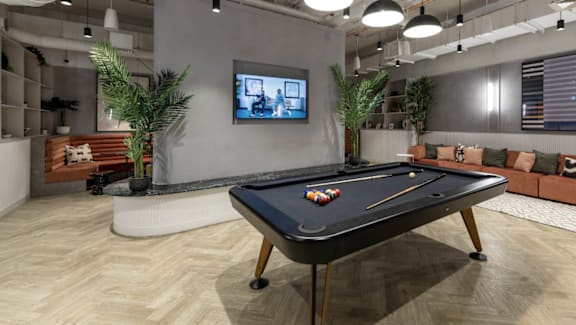 A pool table is in the middle of a room with a couch and a TV.