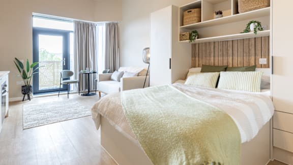 A bedroom with a bed, a chair, and a potted plant.