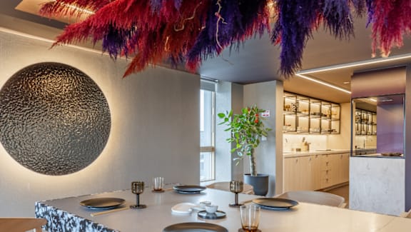 A round wall hanging is on the wall above a dining table.