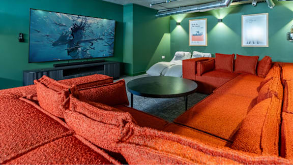 A room with a large orange bed in the foreground and a television in the background.