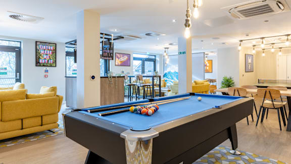 A pool table is in the middle of a room with a yellow couch and a dining table.