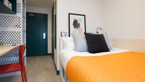 A bed with an orange blanket and two pillows is in the foreground of the image.