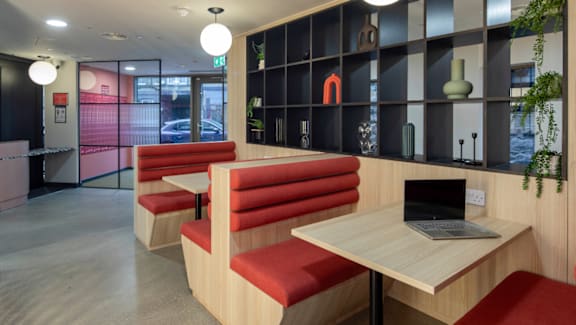A room with a laptop on a table and red chairs.