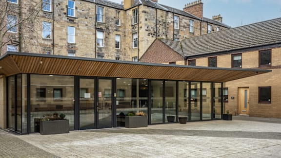 A modern building with a wooden roof and glass walls is in front of an old building.
