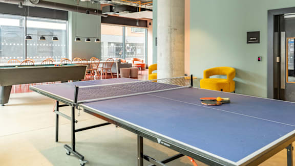 A ping pong table is in the middle of a room with a yellow chair and a door.