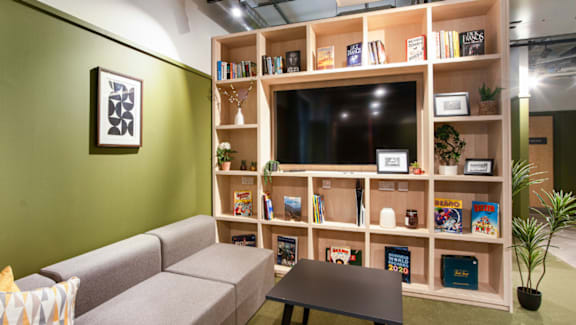A living room with a grey couch, a coffee table, a green wall, a bookshelf, and a plant.