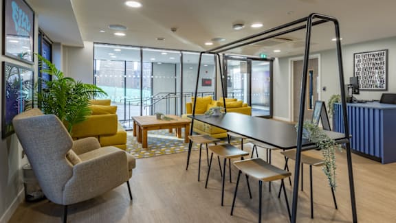 A room with a grey chair and a table with yellow cushions.