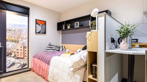 A bedroom with a bed, desk, and a window with a view of the city.