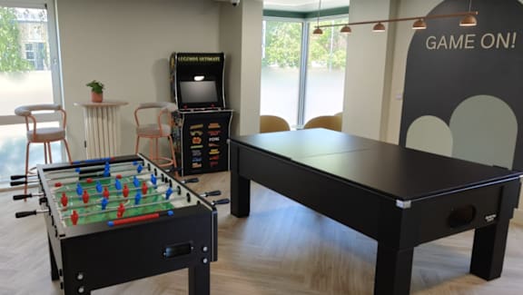 A black air hockey table is in a room with a foosball table and a TV.