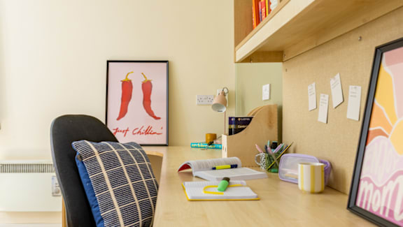 A chair is in front of a desk with a picture of two chili peppers on the wall.