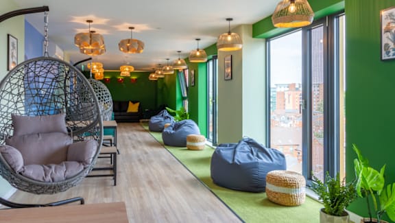 A room with green walls and a long wooden table with a hanging chair and bean bag chairs.