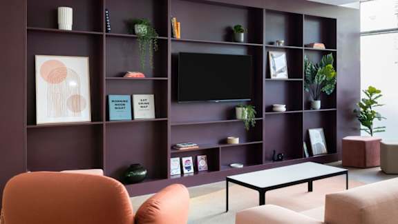 A living room with a purple wall and a flat screen TV.