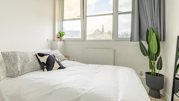 A bed with a white comforter and a pillow with a black and white pattern.