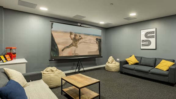 A living room with a grey couch, a wooden coffee table, and a large screen on the wall.