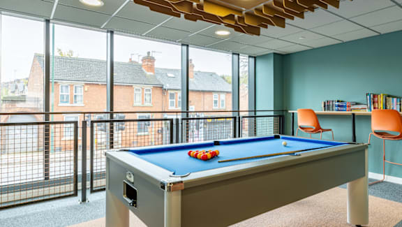 A pool table with orange pool balls and a green cloth is in the middle of a room with a balcony.